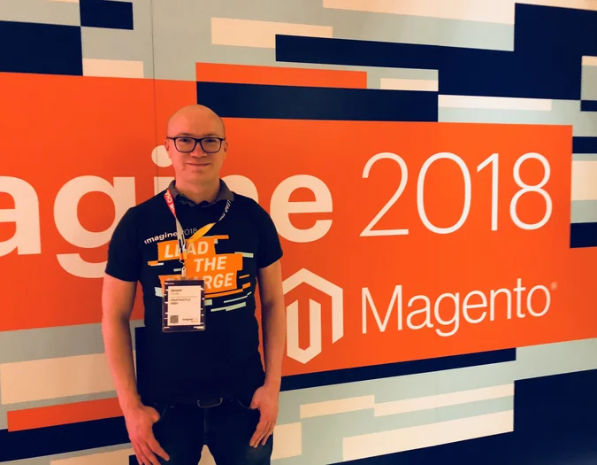 CEO Jaromir posiert vor einer orangefarbenen „Imagine 2018 Magento“ Event-Wand und trägt ein passendes „Lead the Charge“ T-Shirt