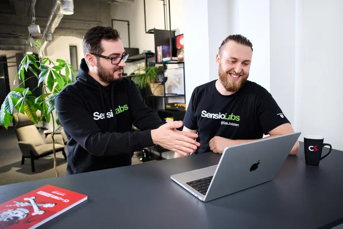 Two developers in SensioLabs shirts discussing something together at a laptop in the office