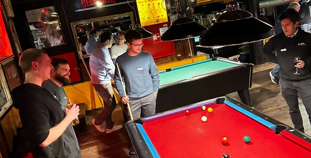 Eine Gruppe von Personen spielt Billard in einer Bar an einem roten Billardtisch