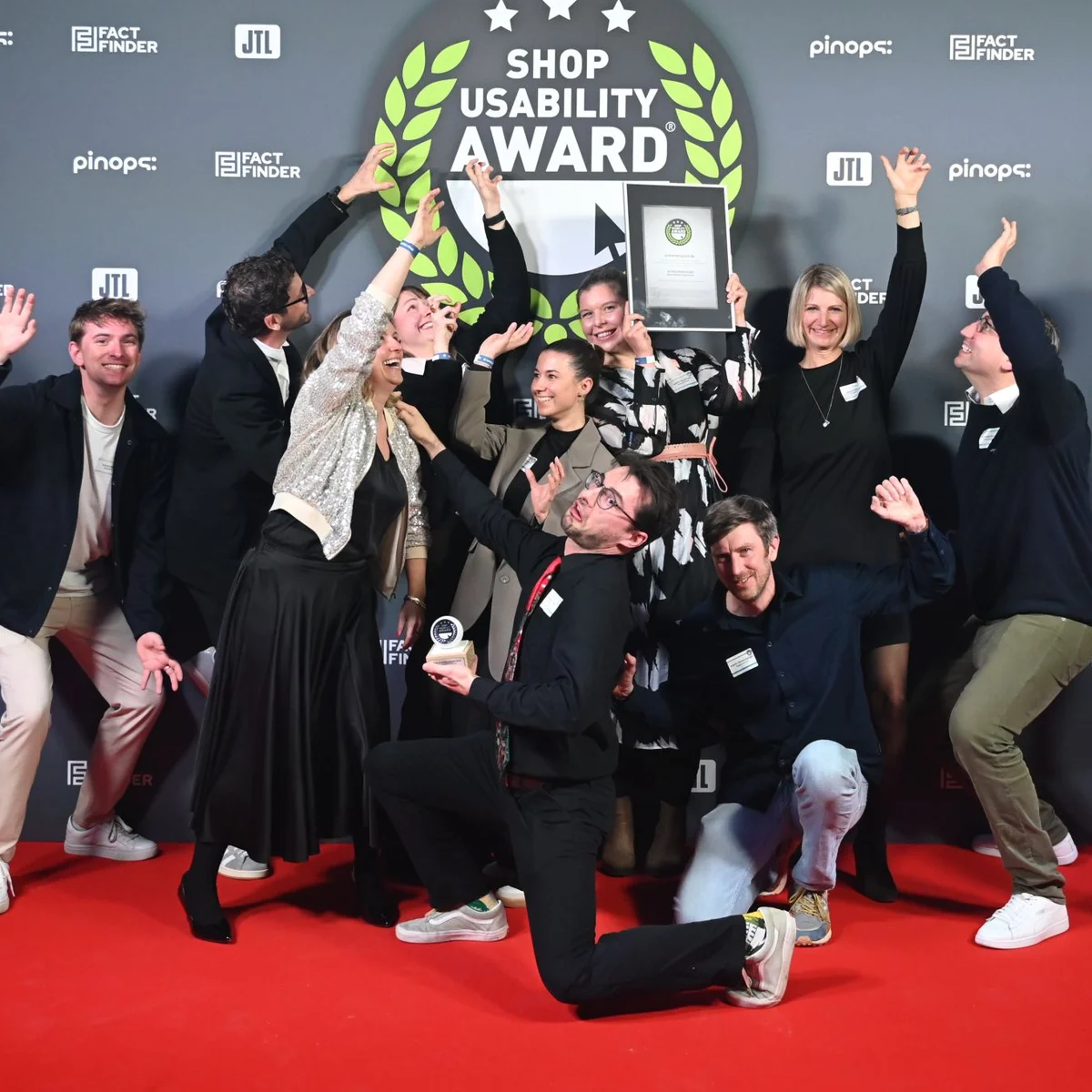 A group of people celebrating on a red carpet with an award, under a "Shop Usability Award" banner.