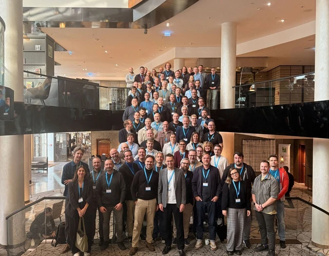 Große Gruppe von Teammitgliedern posiert für ein Gruppenfoto auf einer breiten Treppe in einem modernen Foyer