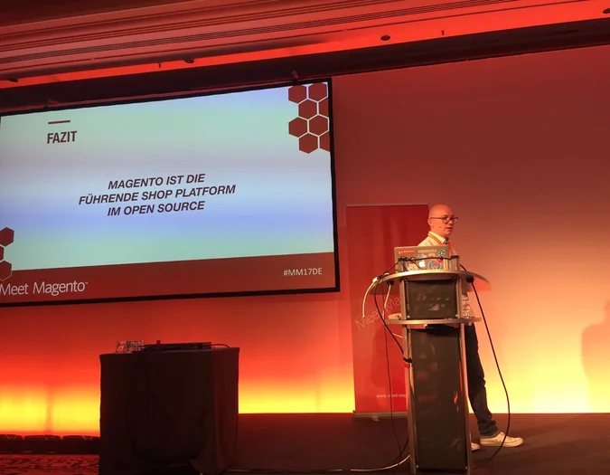 Sprecher bei einem Meet Magento Event präsentiert eine Folie mit dem Titel „FAZIT“ über Magento als führende Open-Source-Shopplattform