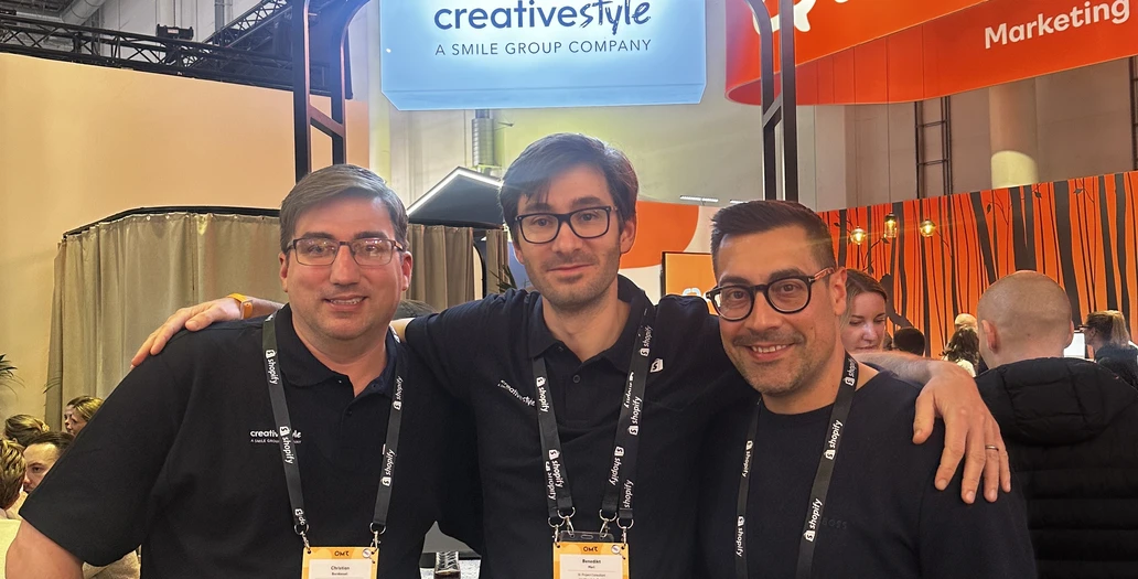 Drei Teammitglieder posieren arm in arm an einem Messestand mit creative style Branding während des OMR Festivals