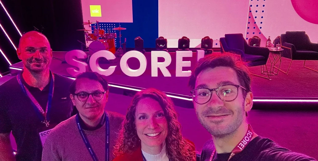 Vier Teammitglieder posieren beim SCORE! Event mit lila Beleuchtung und Bühnen-Branding