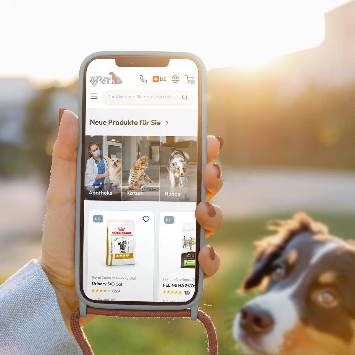 iPet E-Commerce-Website-Vorschau auf einem Smartphone mit neuen Haustierprodukten, darunter Diätfutter von Royal Canin und Purina, vor einem Lifestyle-Hintergrund mit einem Hund im Freien