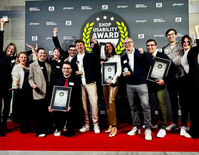 A group of people celebrating on a red carpet, holding awards in front of a "Shop Usability Award" backdrop.