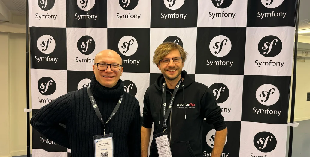 Zwei Männer posieren vor einer schwarz-weiß karierten Symfony-Logo-Rückwand